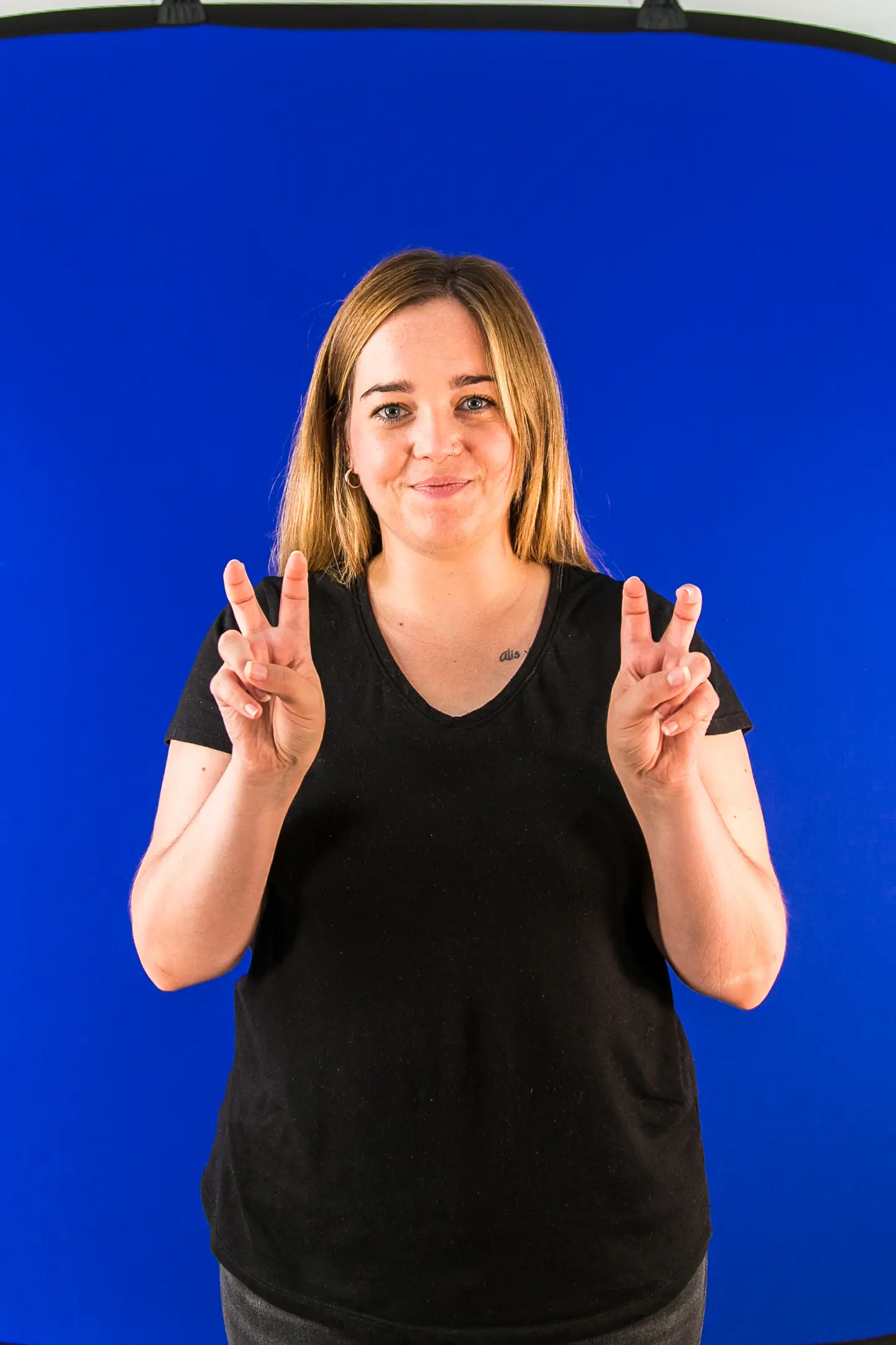 La Cynthia fa el signe TEMA davant un croma blau, somriu i du posada una samarreta negra